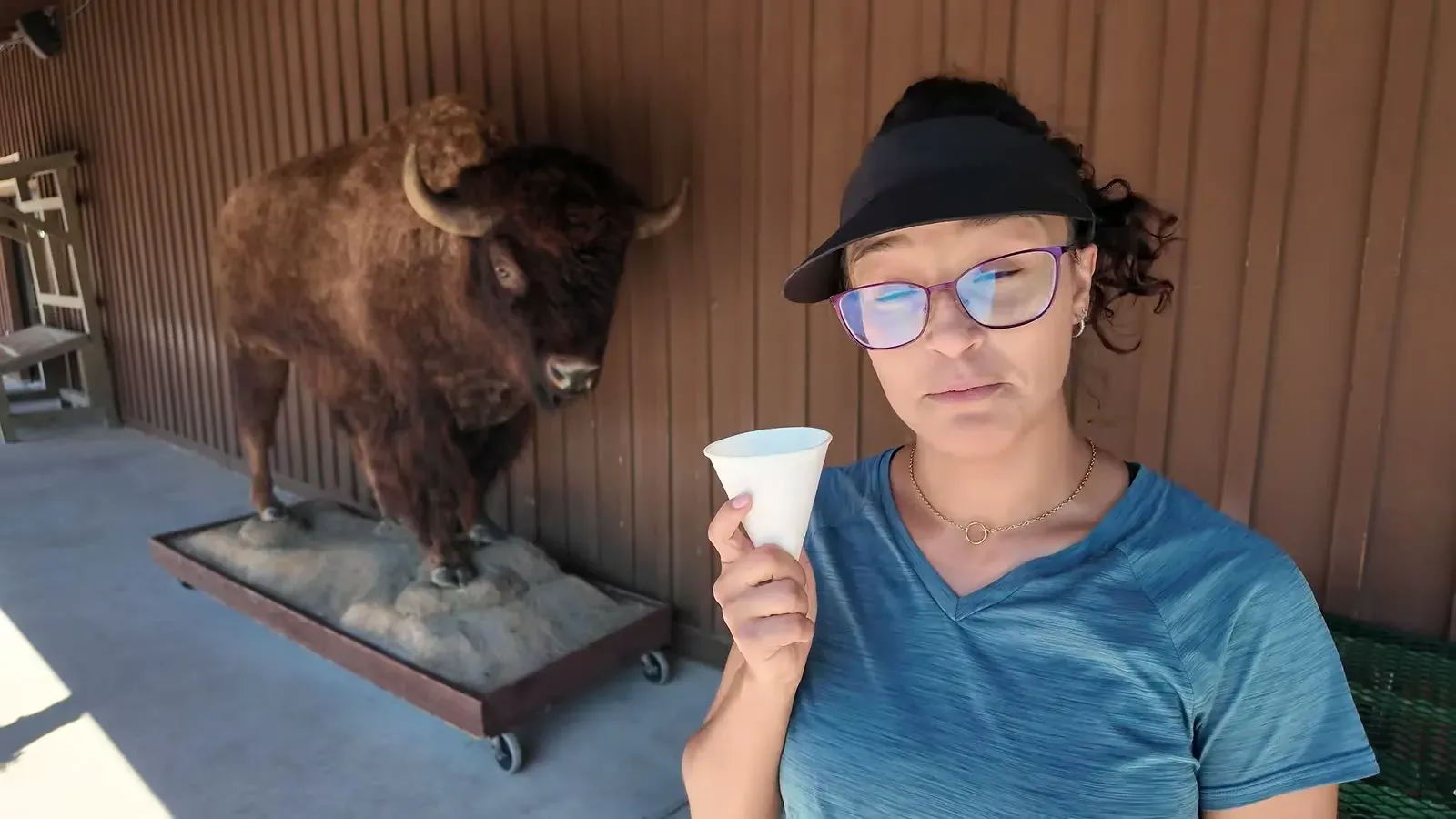 Fabiola drinking a cup of the free ice water at Wall Drug, standing beside a mounted bison