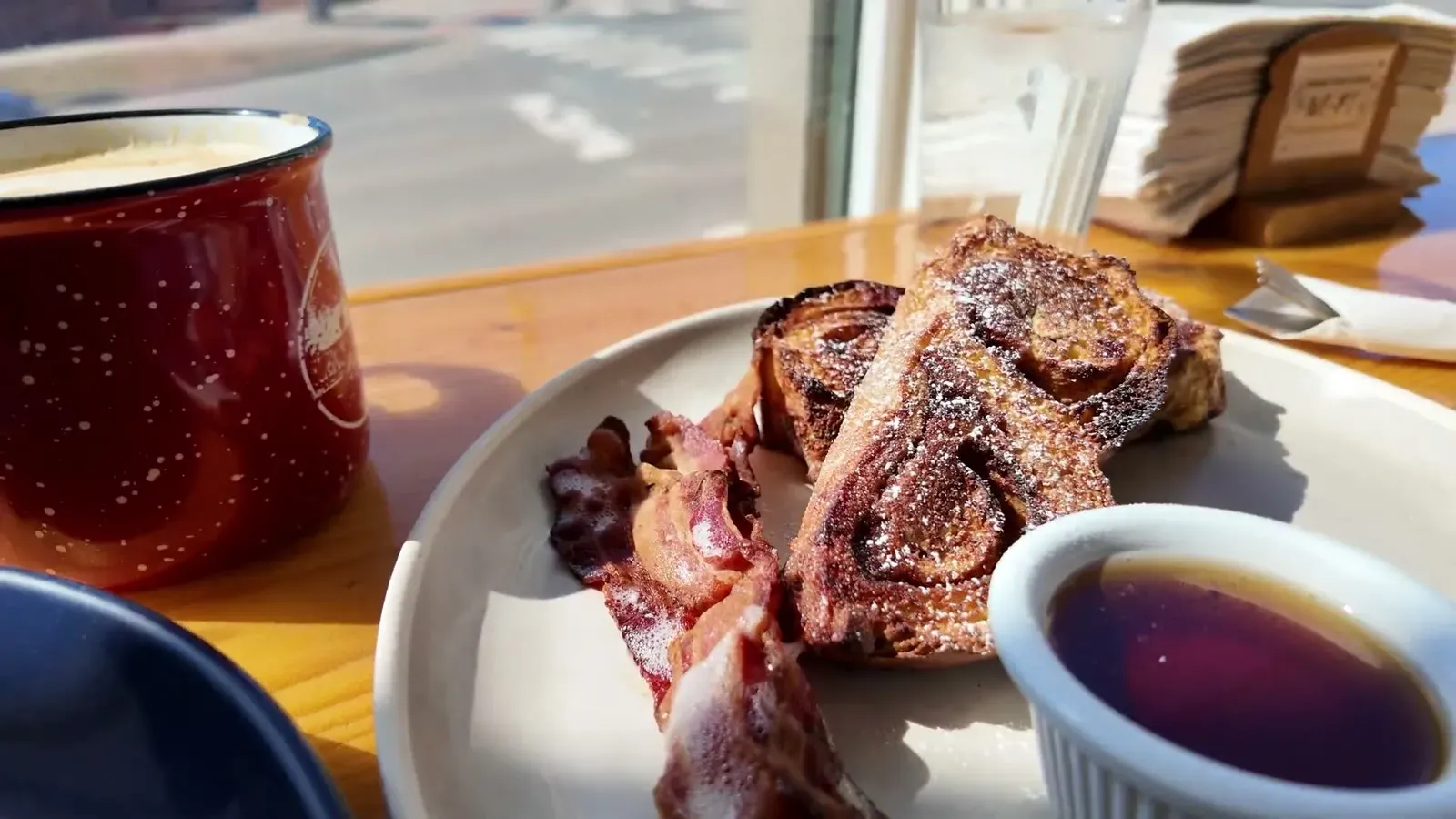 Cinnamon sugar french toast with a side of bacon and maple syrup, coffee in a red enamel mug alongside.