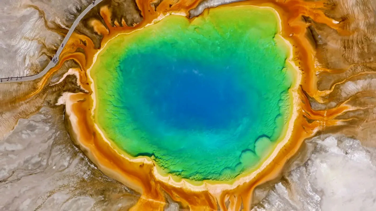 Grand Prismatic Spring seen from above, a deep blue center ringed by bands of green, yellow and orange