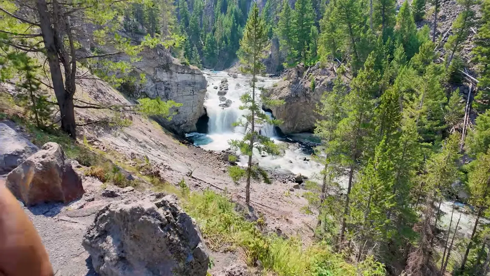 A waterfall dropping through the rocky, pine-lined walls of Firehole Canyon with nobody else around
