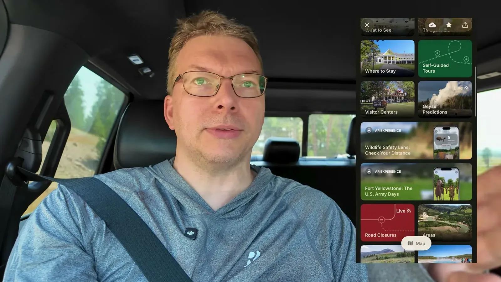 Nathan in the truck holding up a phone showing the National Park Service app open on Yellowstone, with geyser predictions and visitor centers listed