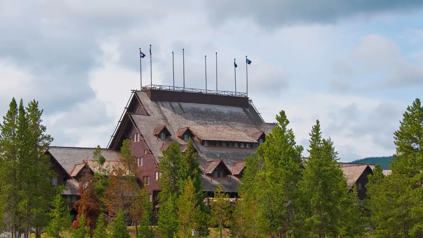 The Old Faithful Inn, a large timber hotel with steep shingled roofs and flagpoles, standing among pines inside the park