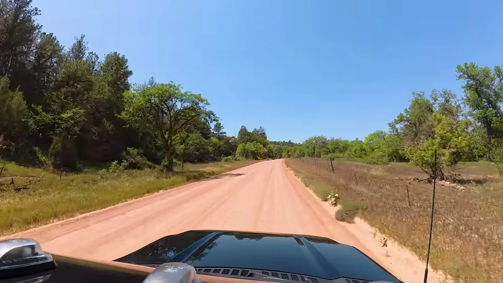 A narrow red dirt back road running between trees and a fence line, the route Google Maps chose toward Wind Cave