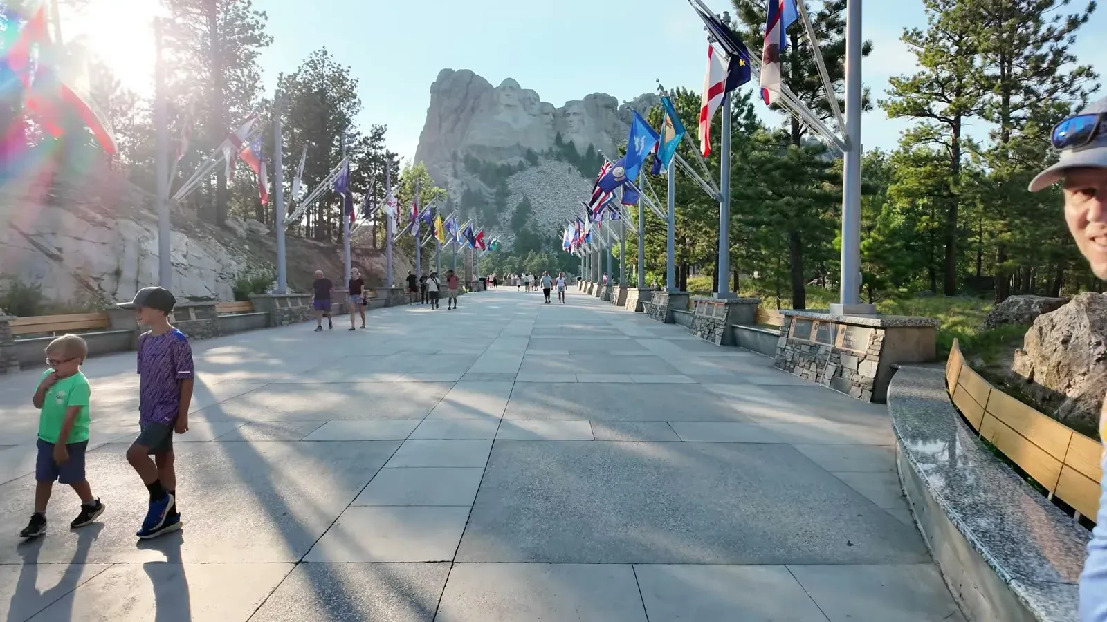 The Avenue of Flags at Mount Rushmore in low evening sun, with only a handful of visitors on the walkway