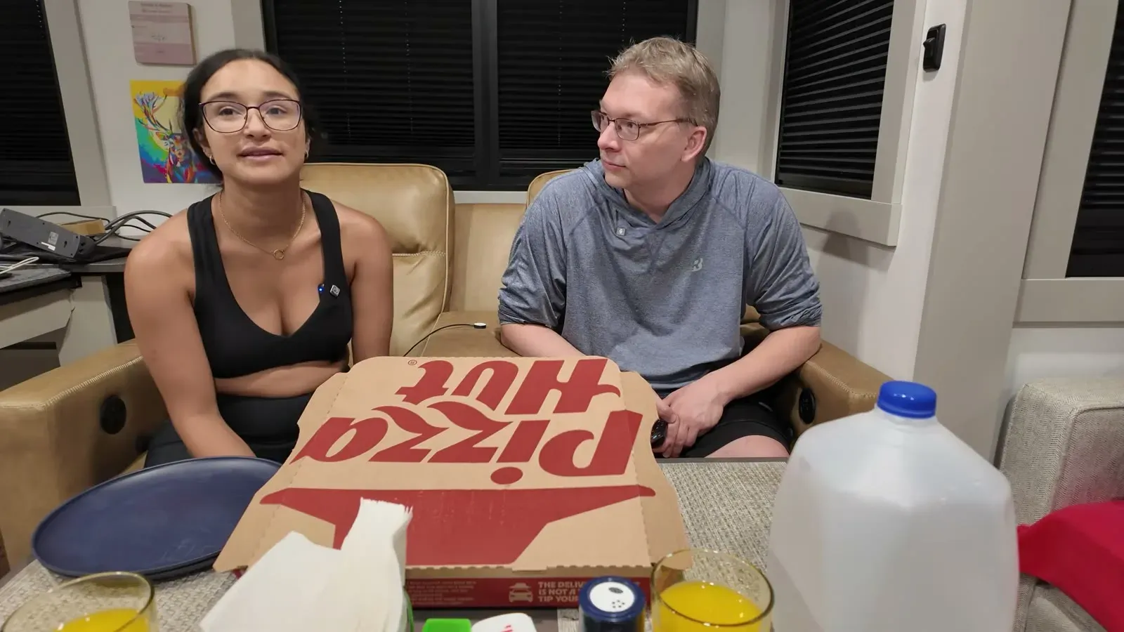 Nathan and Fabiola back inside the RV with a pizza box open on the table in front of them