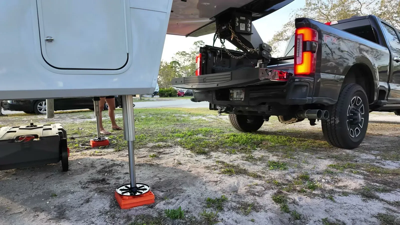 The Brinkley's front leveling jack resting on an orange block with the truck hitched up behind it so the whole hydraulic system could come in for the jack swap.