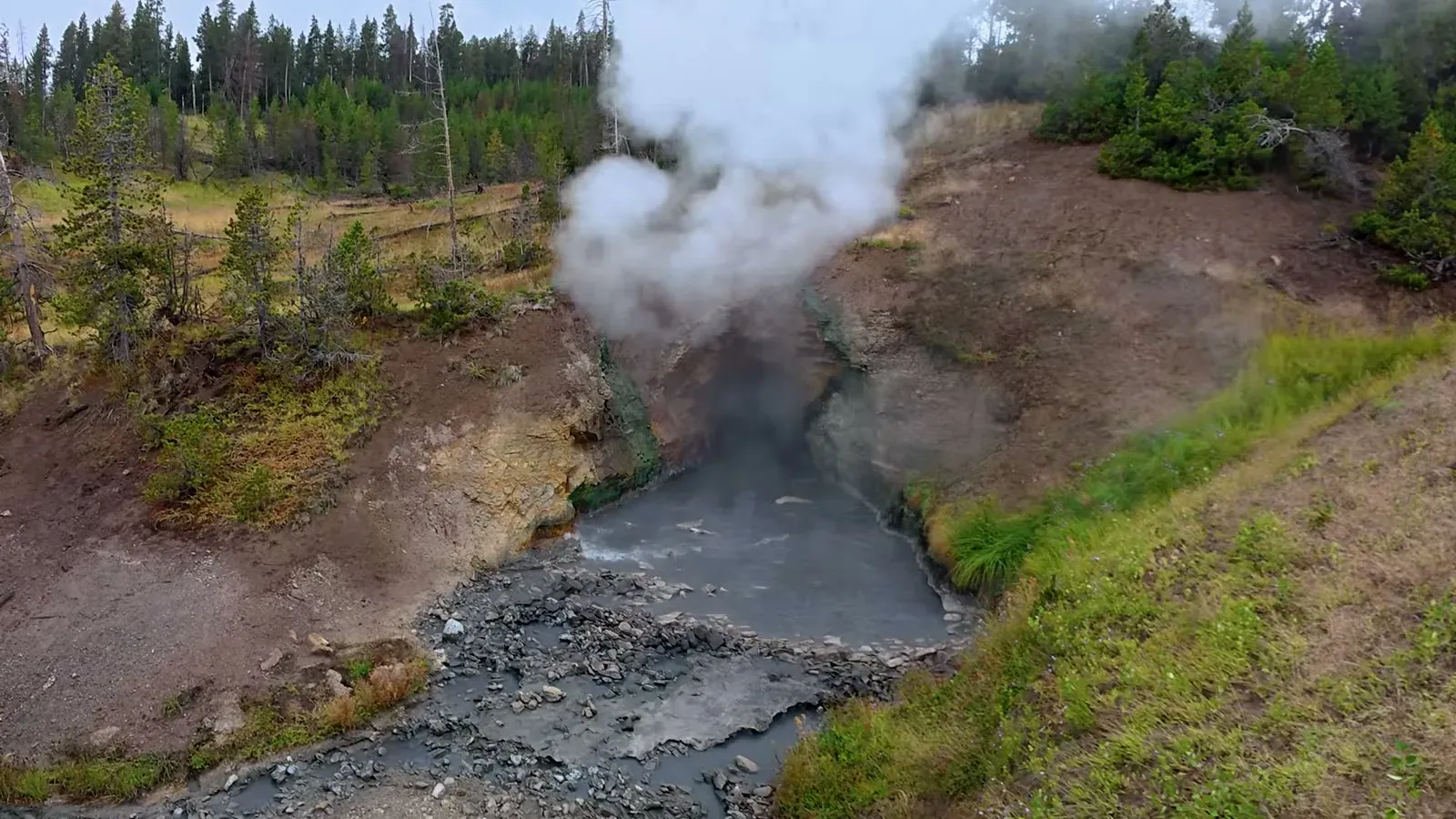 Steam pouring out of a vent above a gray pool in the Mud Volcano area on a cloudy day