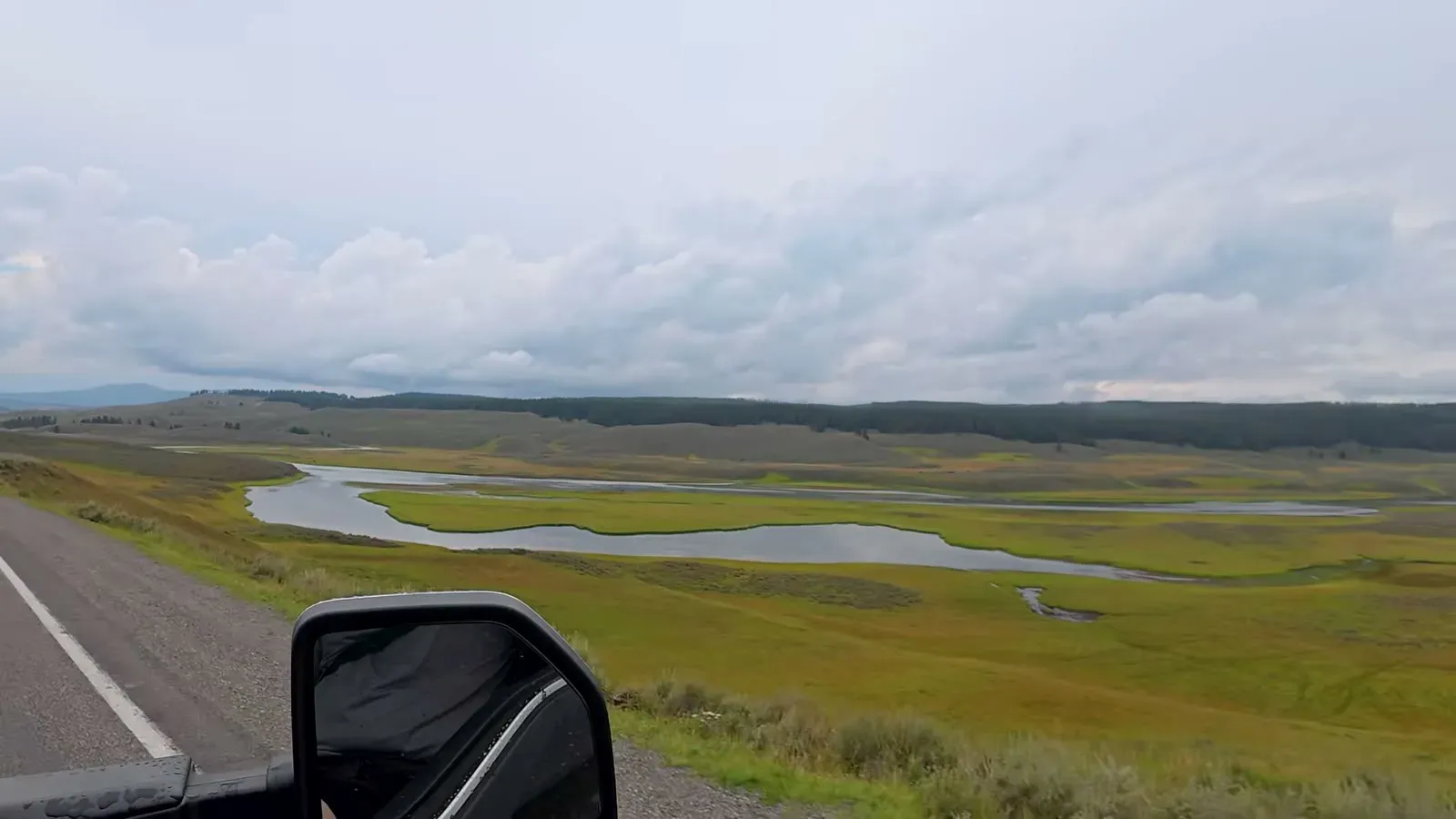 The Yellowstone River winding through the wide green grassland of Hayden Valley under gray clouds