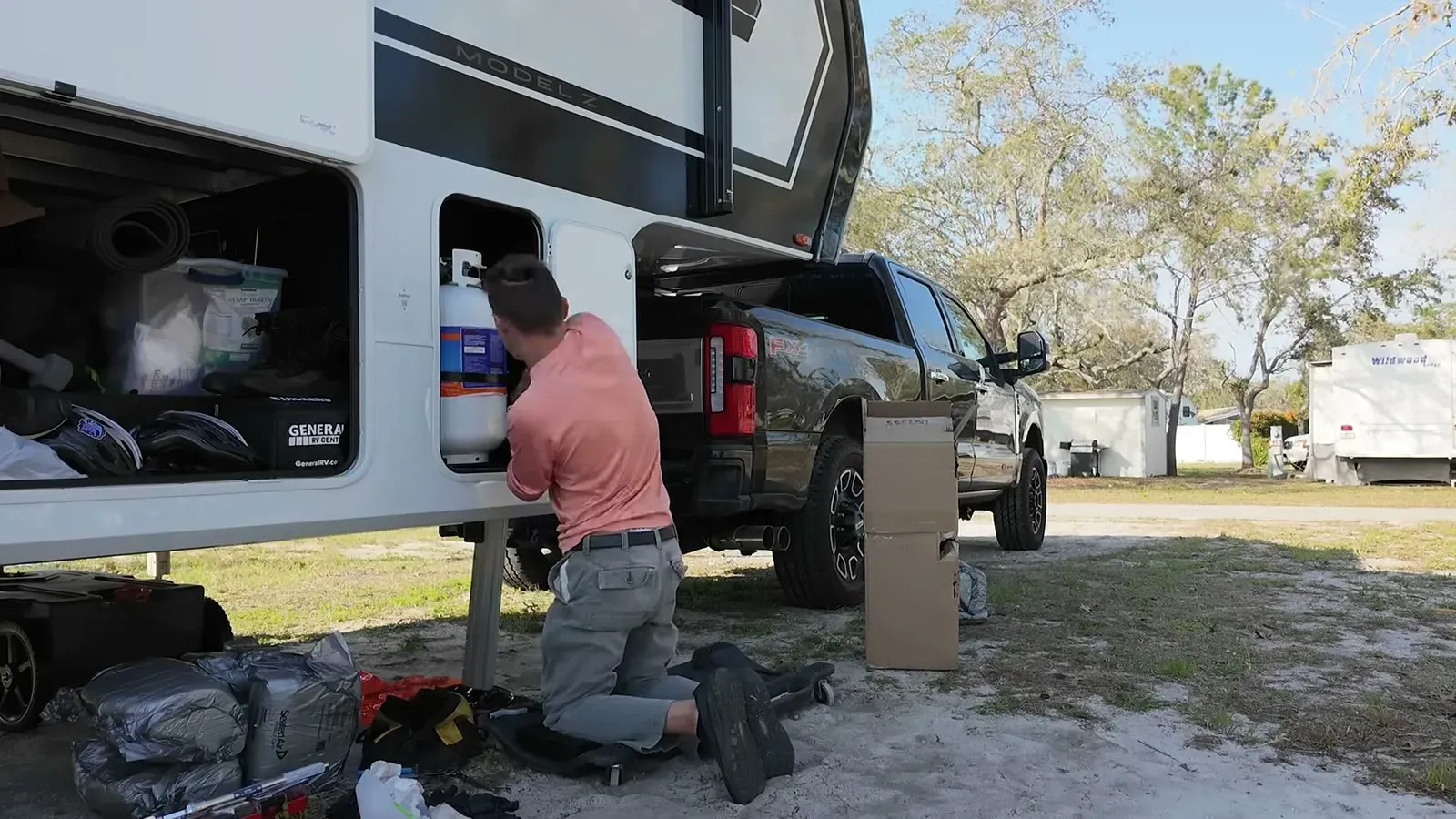 Our mobile tech kneeling at the Model Z's propane bay, where the connector for the leaking jack lives, with parts boxes staged by the truck.
