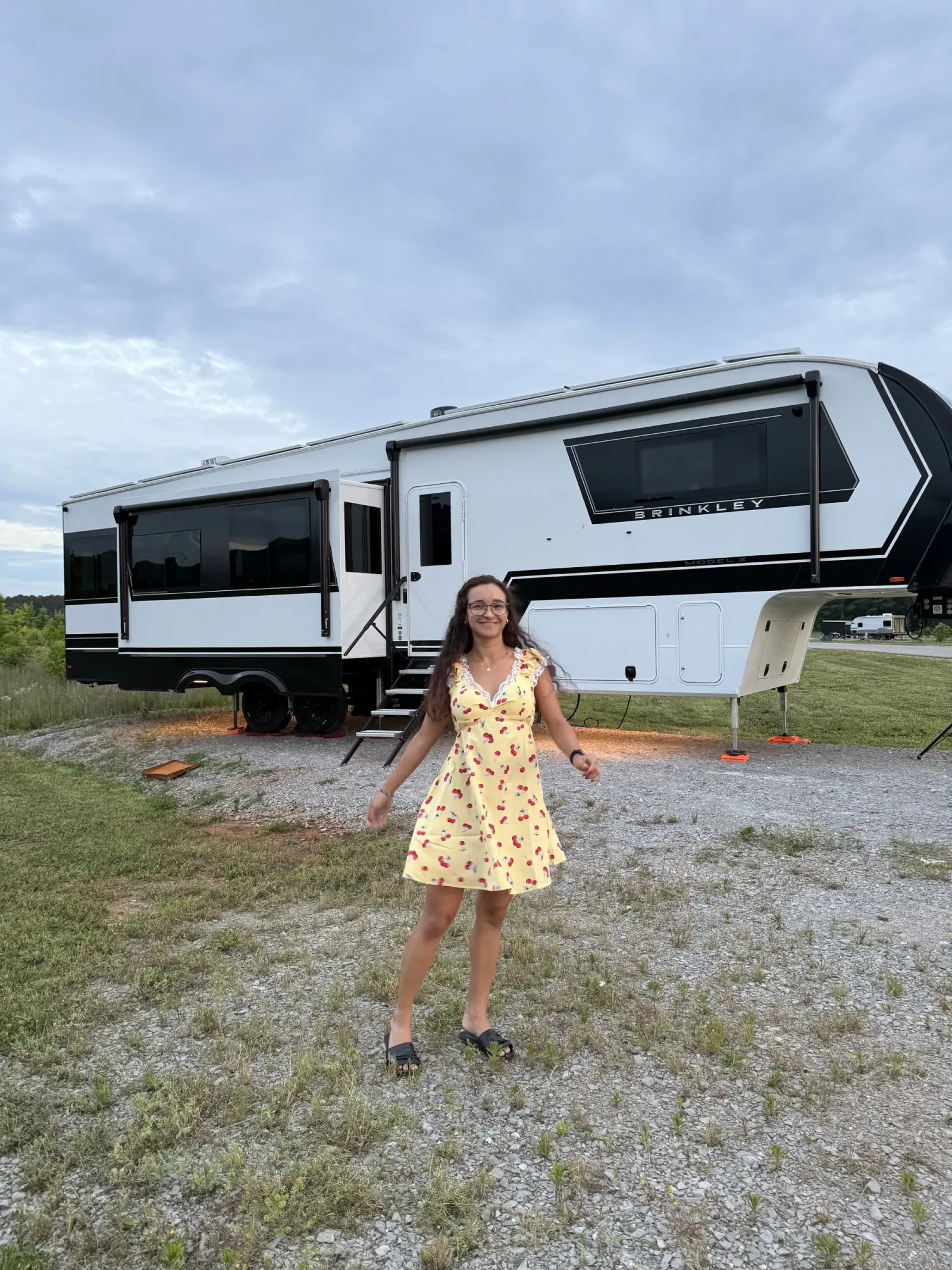 Fabiola in a yellow dress in front of our Brinkley fifth wheel on its gravel site at Ditto Landing in Huntsville