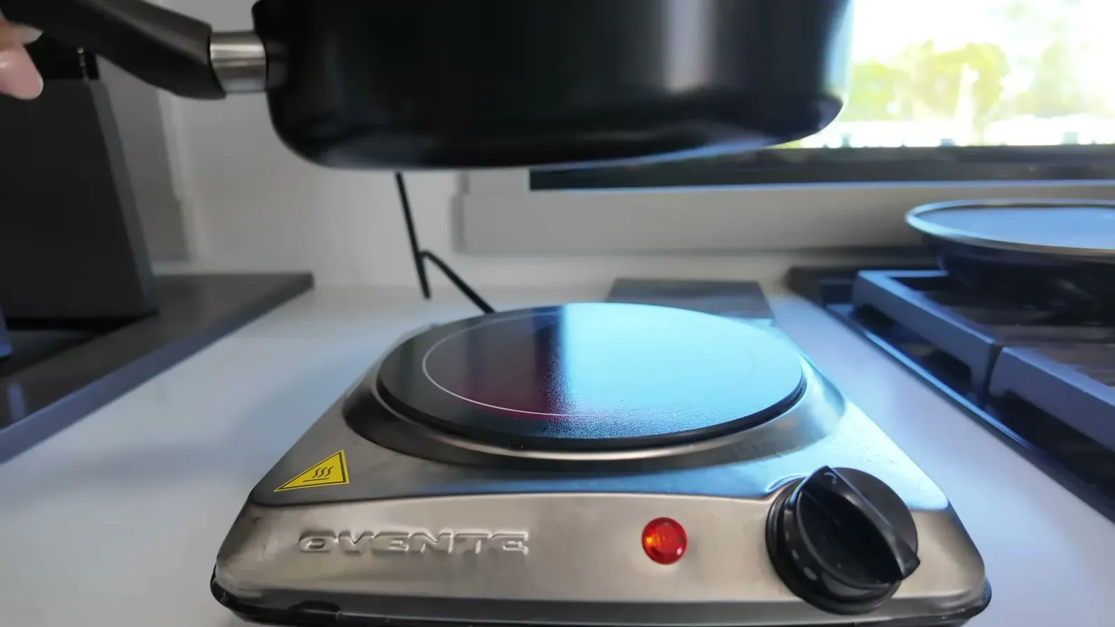 Lifting a pan over the little Ovente electric burner on the kitchen counter, indicator light glowing, running off our solar instead of propane.