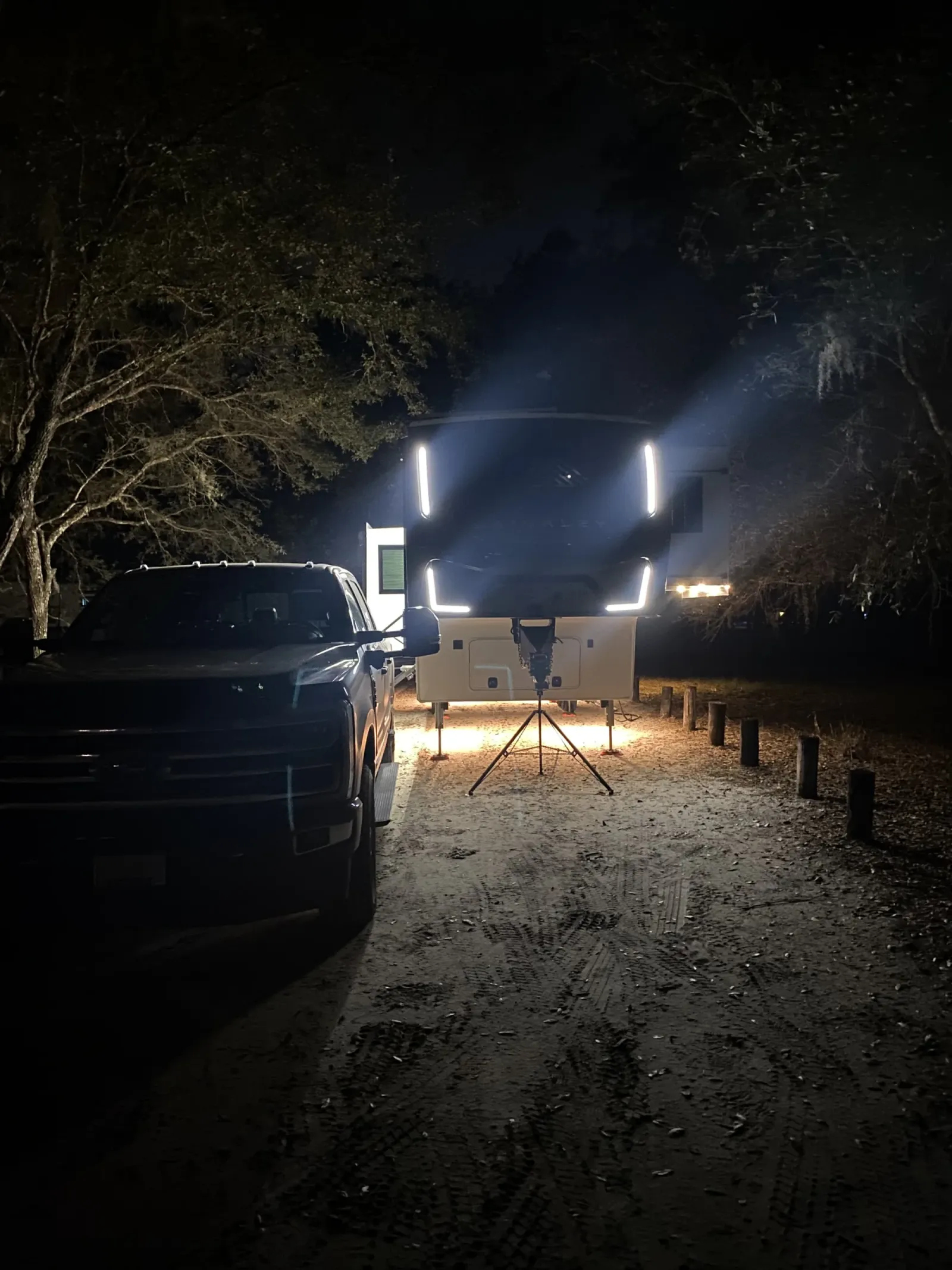 Our fifth wheel backed into its Moss Park site at night, the truck beside it and wooden posts close along the edge of the pad
