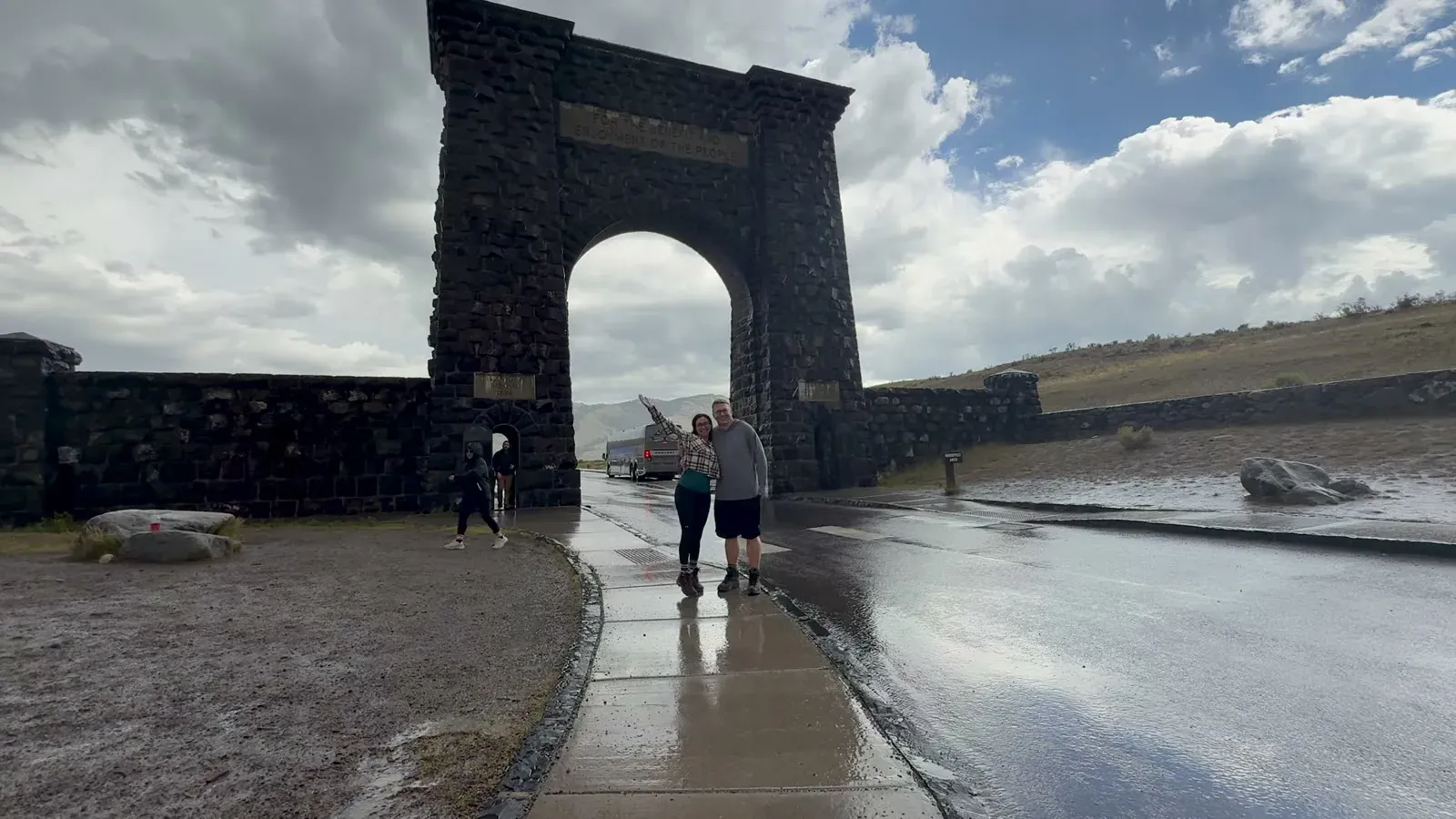 Nathan and Fabiola posing under the Roosevelt Arch on a wet, cloudy afternoon
