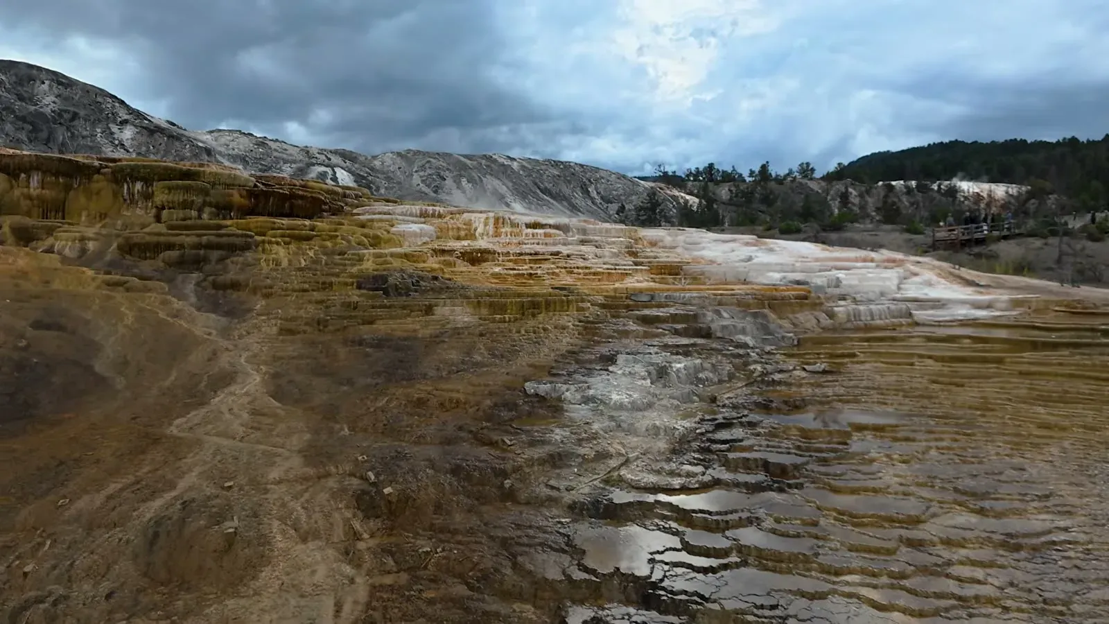 Orange and white travertine terraces stepping down the hillside at Mammoth Hot Springs under a stormy sky