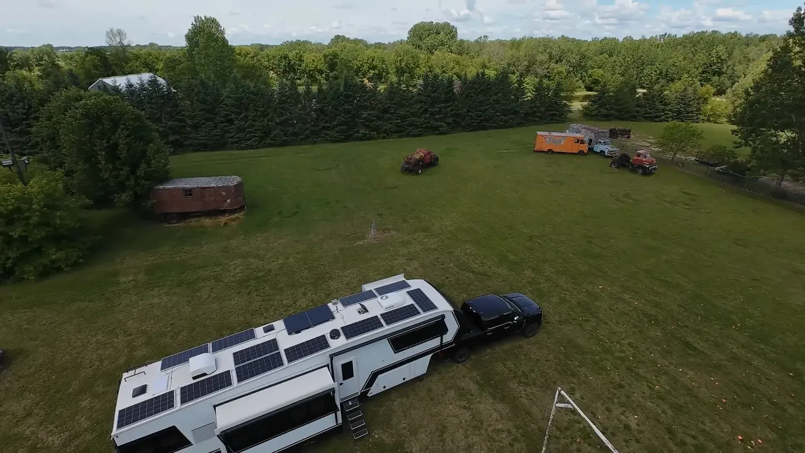 Drone view of our fifth wheel parked on the grass at Rays Boneyard Saloon in Lena, Wisconsin, our first Harvest Hosts stay, with old trucks and trailers in the field