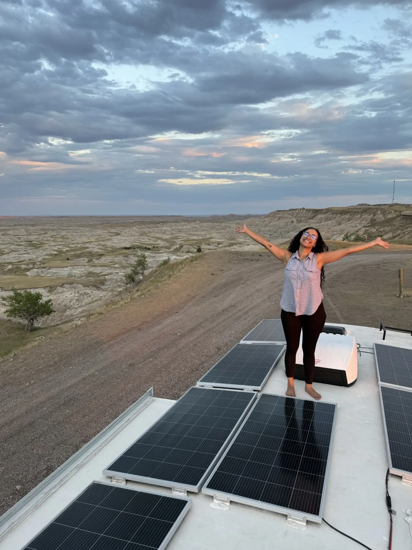 Fabiola with her arms raised on the roof of our Brinkley, surrounded by the solar panels from our upgrade