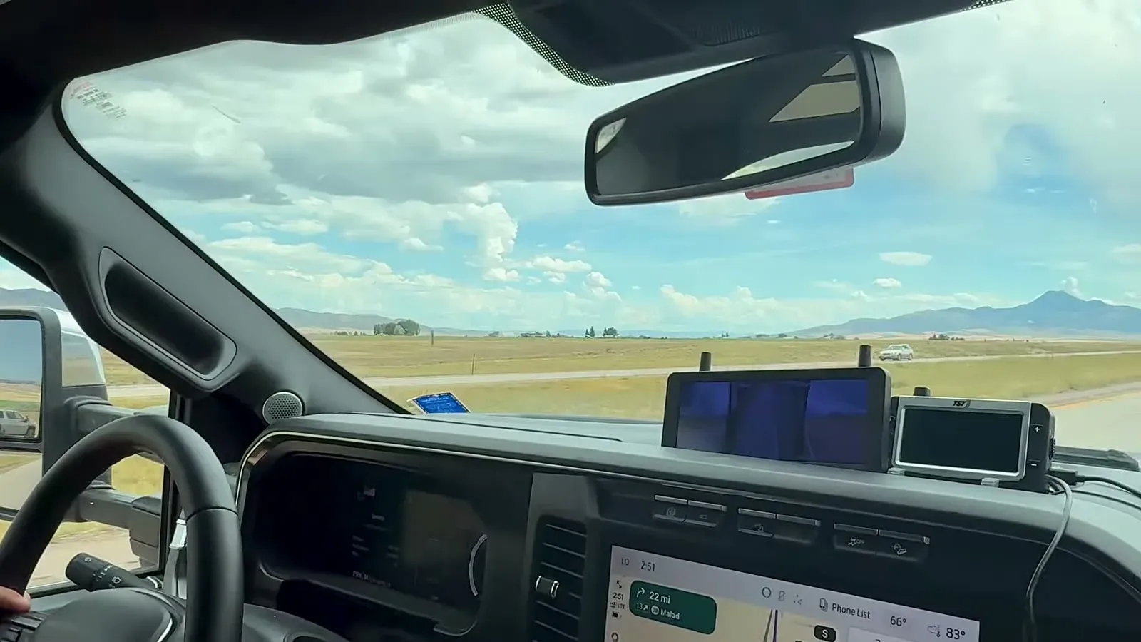 The CampSync monitor on the dash of our truck while we tow across a wide, flat valley with mountains on the horizon