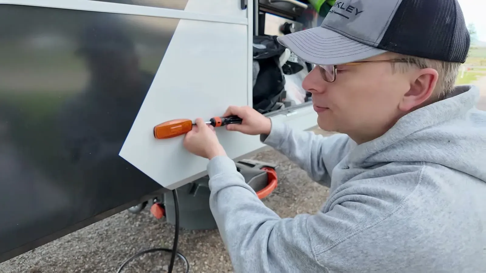 Nathan working a screwdriver into the white side panel of the fifth wheel where an amber marker light comes off