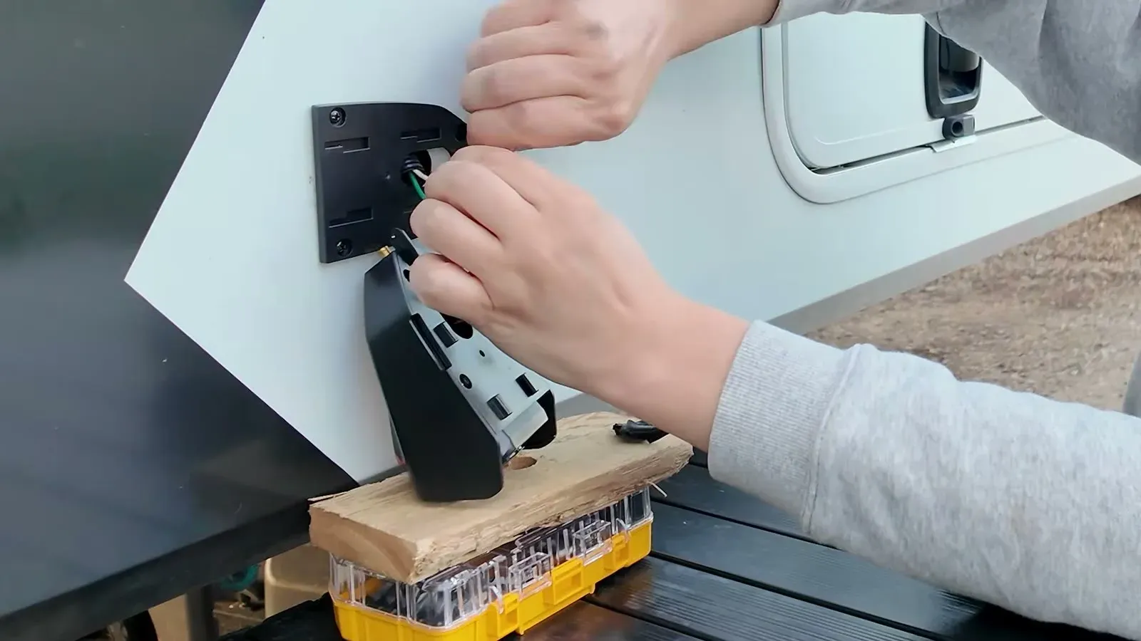Connecting a CampSync side camera to the old marker light wiring, with the camera propped on a block of scrap wood on our folding table