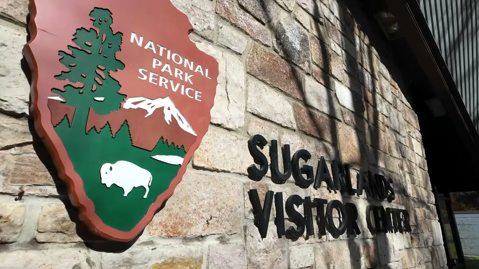 The National Park Service arrowhead sign on the stone wall at the Sugarlands Visitor Center entrance.