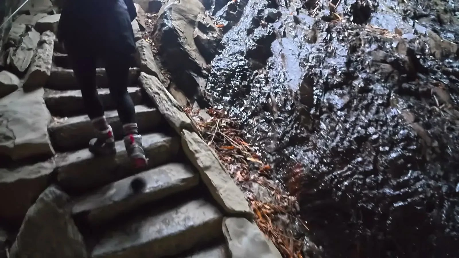 Fabiola climbing the narrow stone stairs cut through Arch Rock, with wet rock glistening beside the steps.