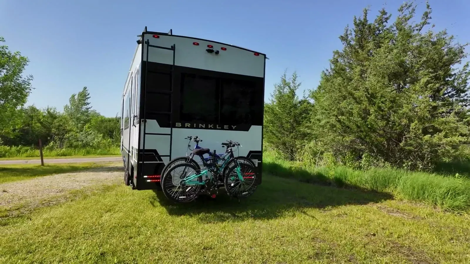 The back of our Brinkley fifth wheel, bikes still on the rack, easing off the narrow park road onto the grassy edge of our site at Richard Bong.