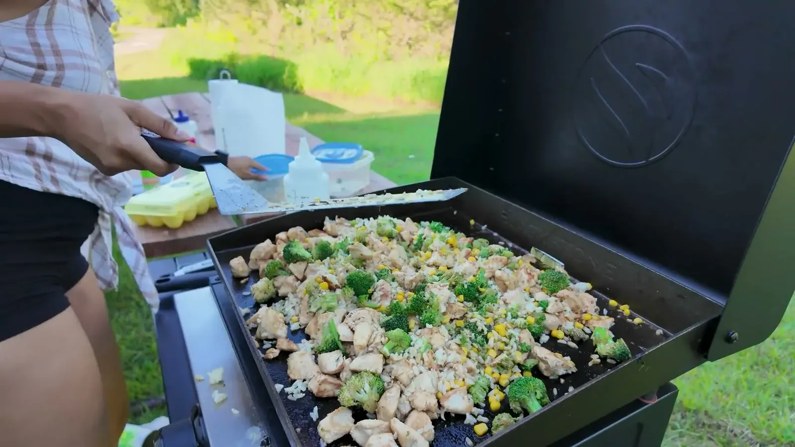 Fried rice loaded with chicken, broccoli, and corn spread across the Blackstone griddle at our campsite, with meal prep containers on the picnic table behind.