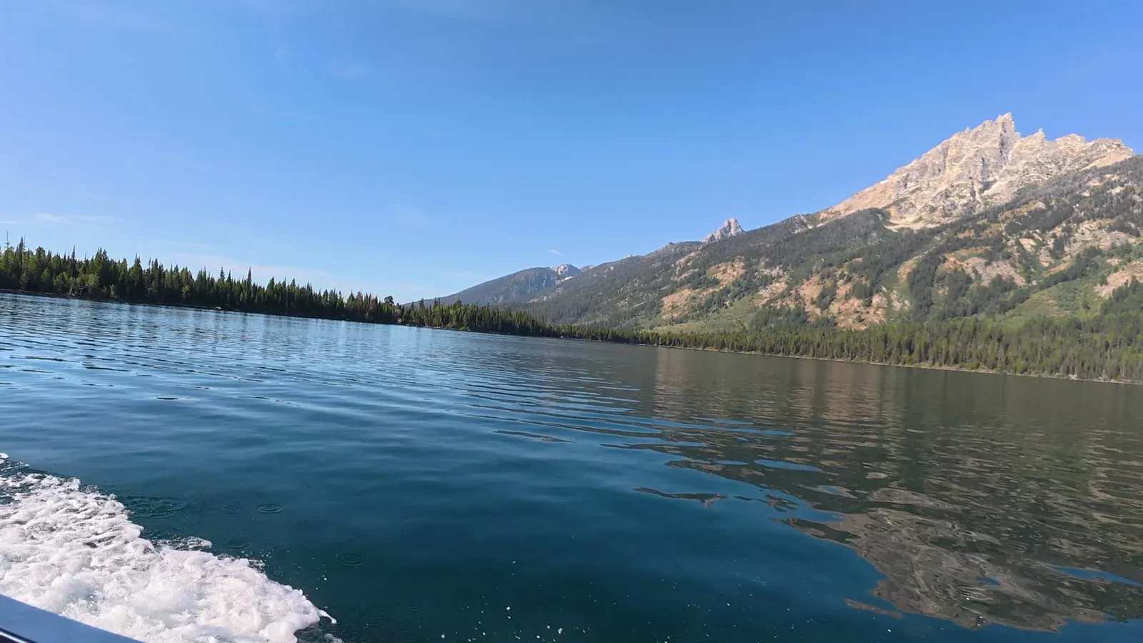 The wake of the boat crossing Jenny Lake in the morning, with a rocky Teton peak above the far shore