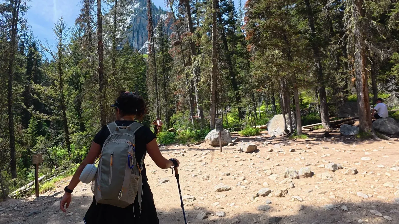 Fabiola with her backpack and trekking poles on a rocky stretch of trail among tall pines