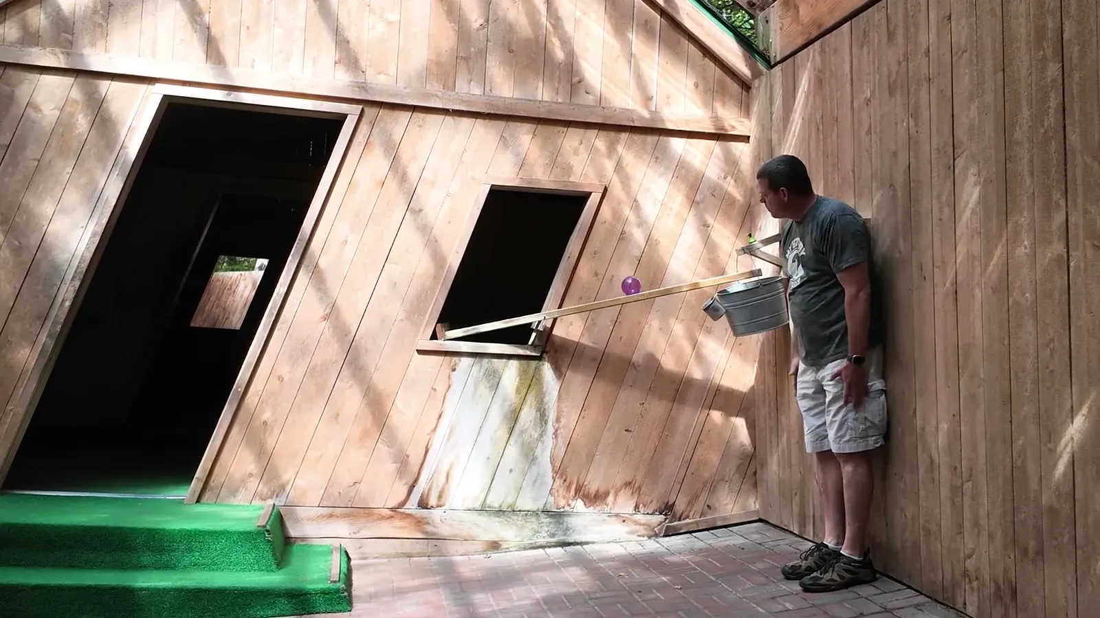 Nathan braces at a strange angle against the wall of the Mystery Spot's tilted cabin while a ball waits at the top of its uphill ramp.