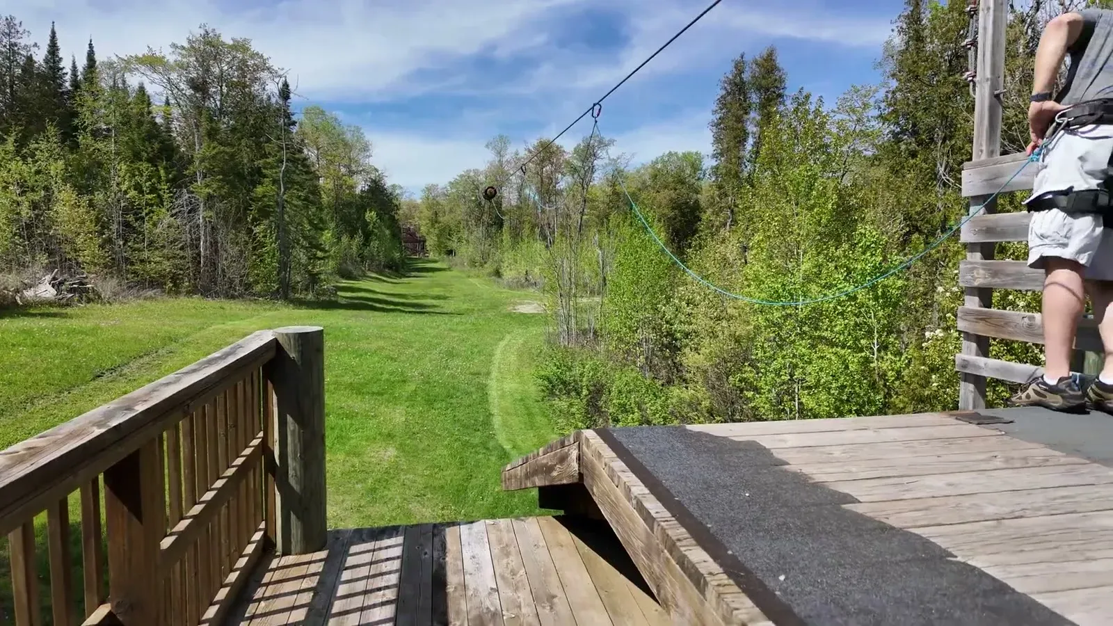 The zip line cable runs from the wooden launch deck down a long green corridor cut through the trees.