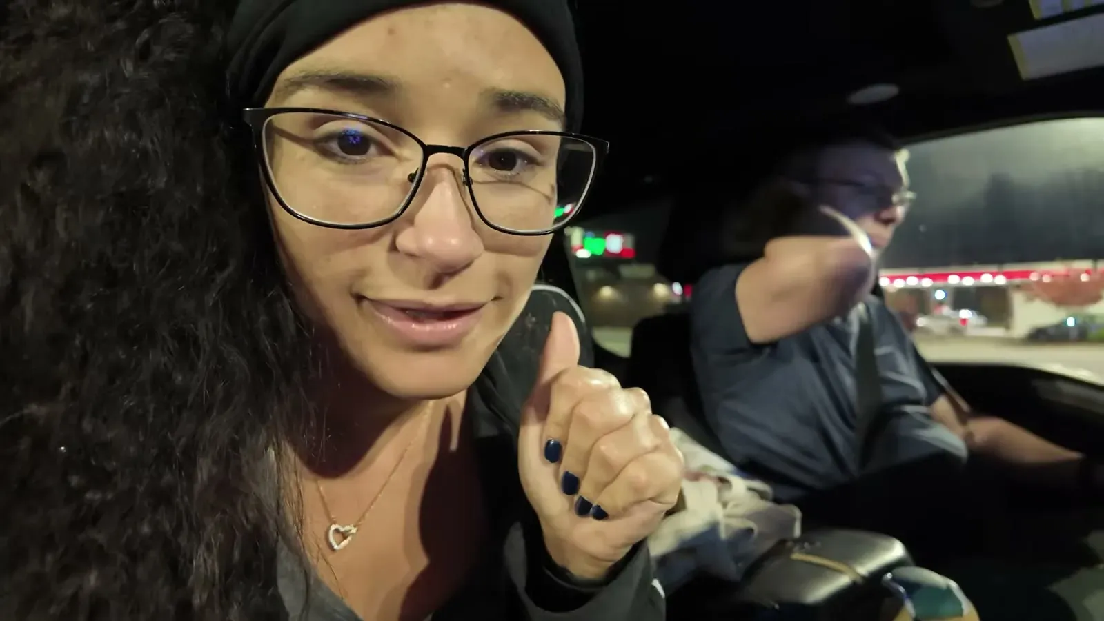 Fabiola gives a thumbs up from the passenger seat while Nathan drives the last dark hour past a lit-up gas station.