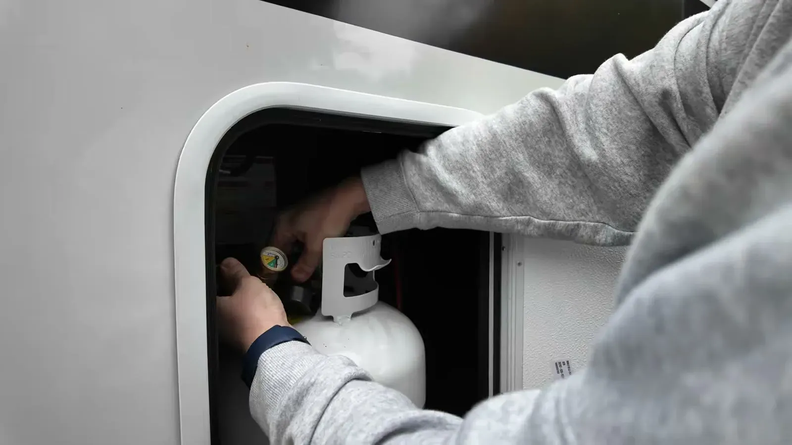 Hooking a freshly filled propane tank back up inside the Brinkley's propane compartment.