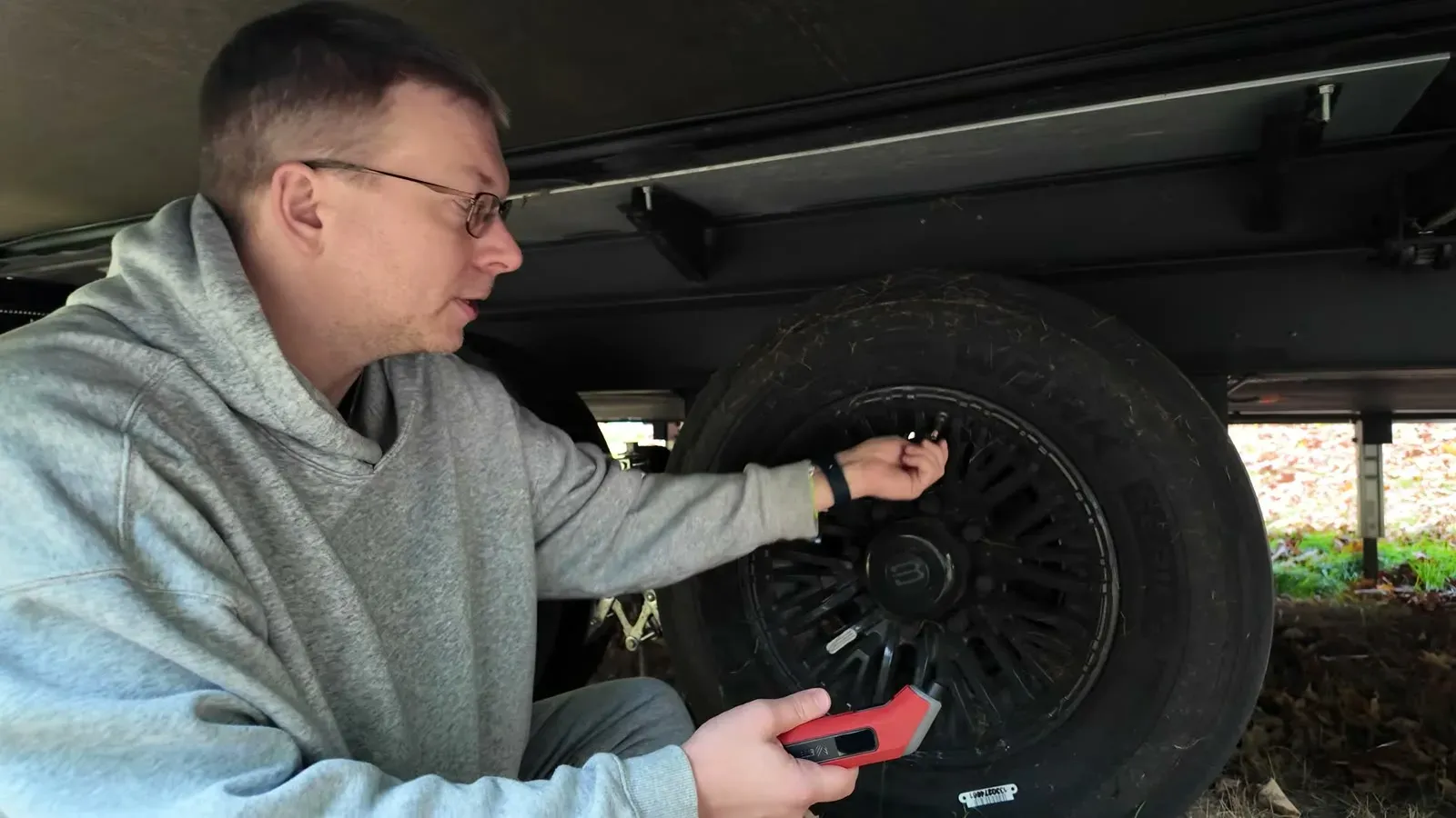 Nathan crouched at a trailer tire, checking the pressure with a digital gauge before travel.