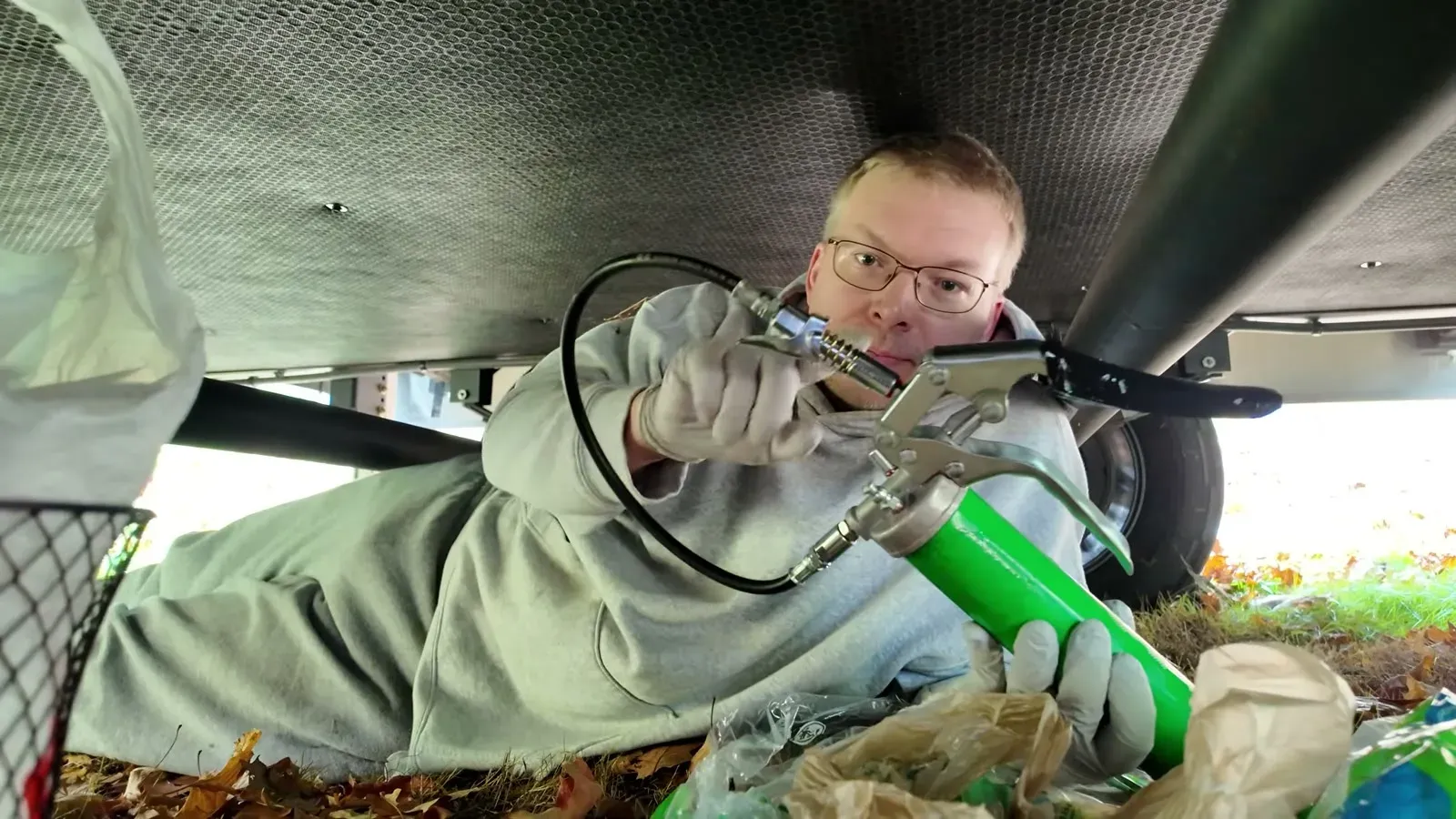 Nathan under the trailer with the LockNLube grease gun, working through the wet bolt fittings.