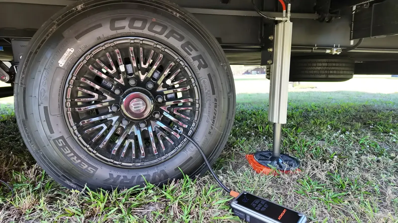 The cordless inflator sits in the grass hooked up to one of the fifth wheel's Cooper tires for a pressure check.