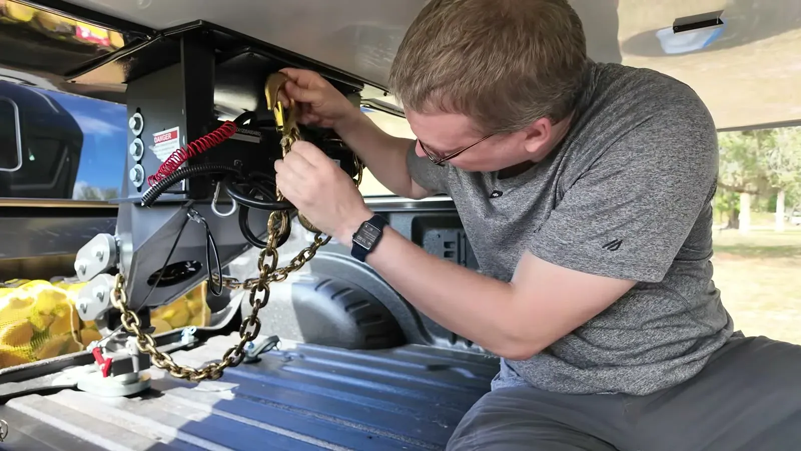 Nathan kneels in the truck bed securing the safety chains on the gooseneck hitch before travel day.