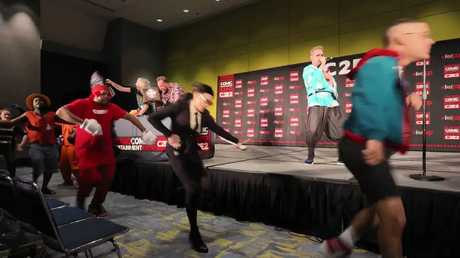 Cosplayers crossing the stage at the C2E2 crew contest, with the red convention backdrop behind them.