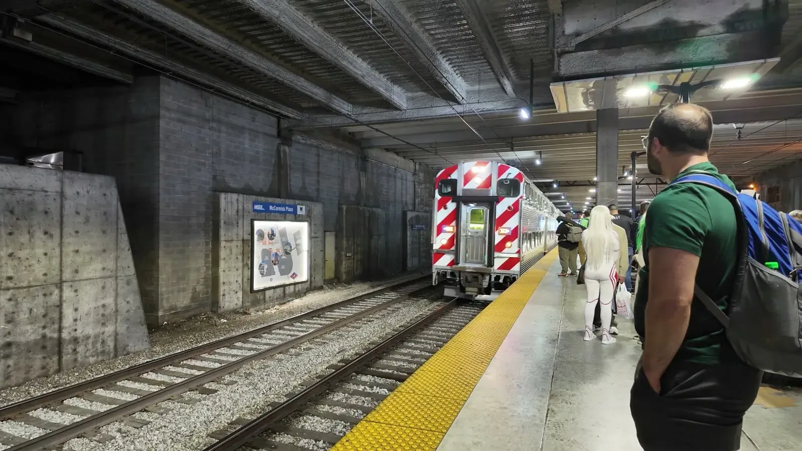 A red and silver Metra bilevel train waiting at the underground platform as riders walk toward the cars.