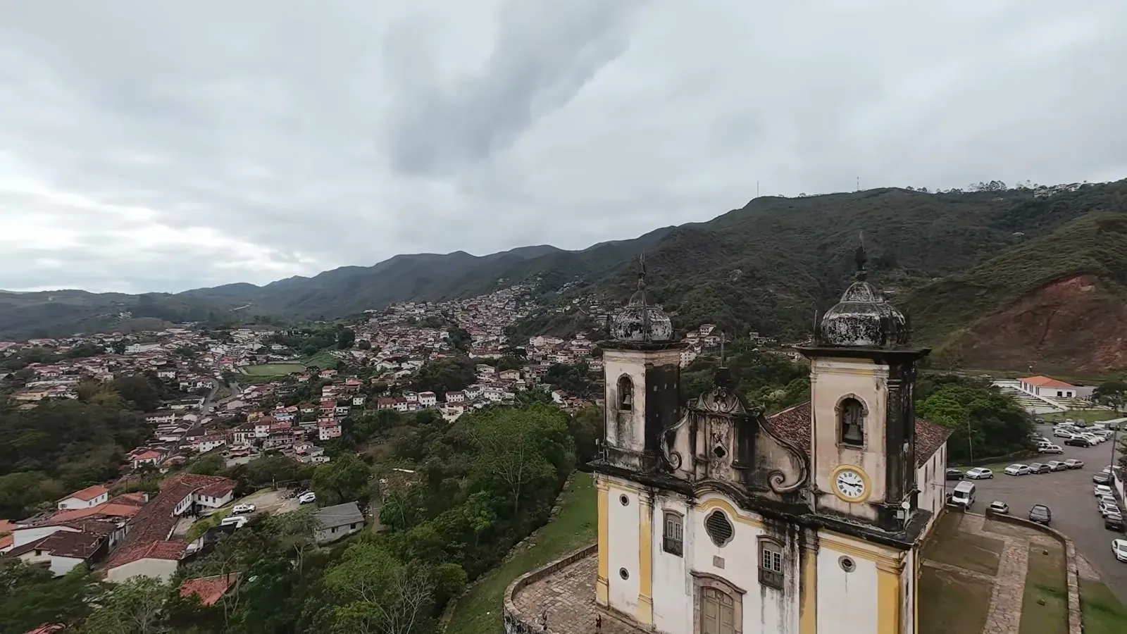 Looking down on a baroque church and the rooftops of Ouro Preto under a low gray sky from the overlook.