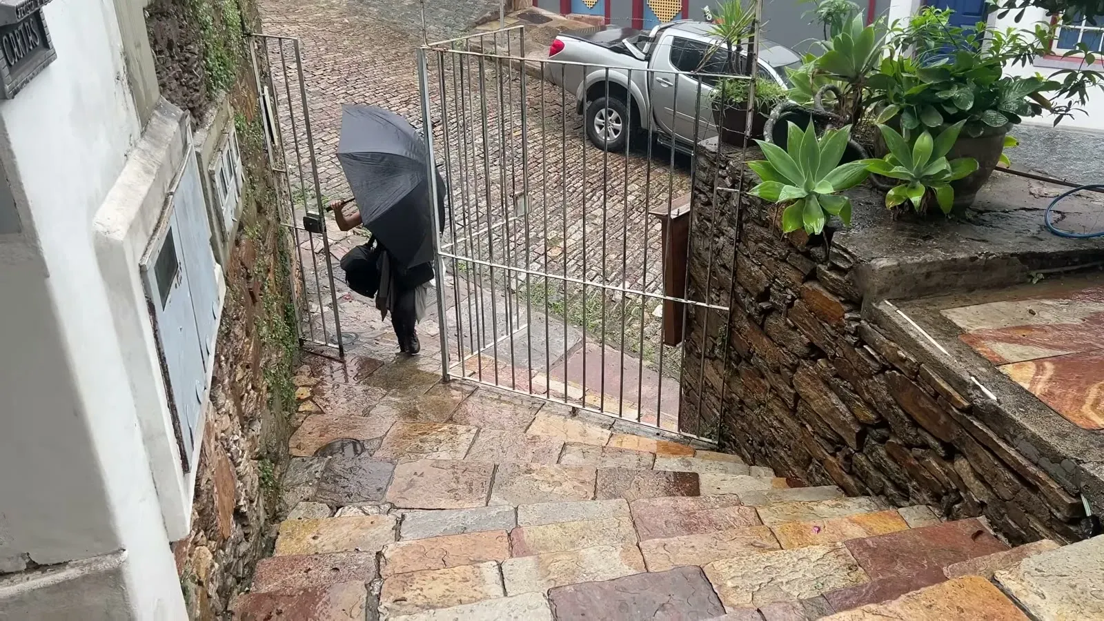 Heading down steep wet cobblestone steps under an umbrella, the kind of descent that earns real grip on your shoes.