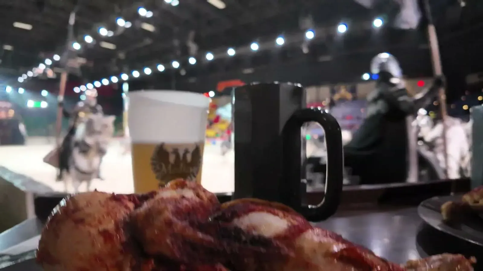 Half a roast chicken and a cold drink on our counter while a knight rides past the arena rail just beyond our seats.