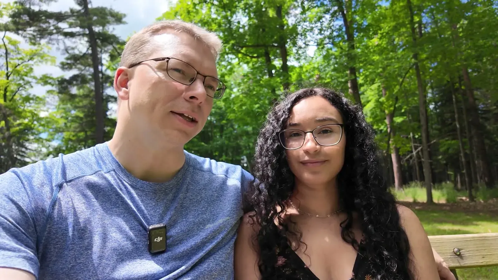 Nathan and Fabiola on a shaded bench in the woods, talking through why the fifth wheel needs a one-ton truck.