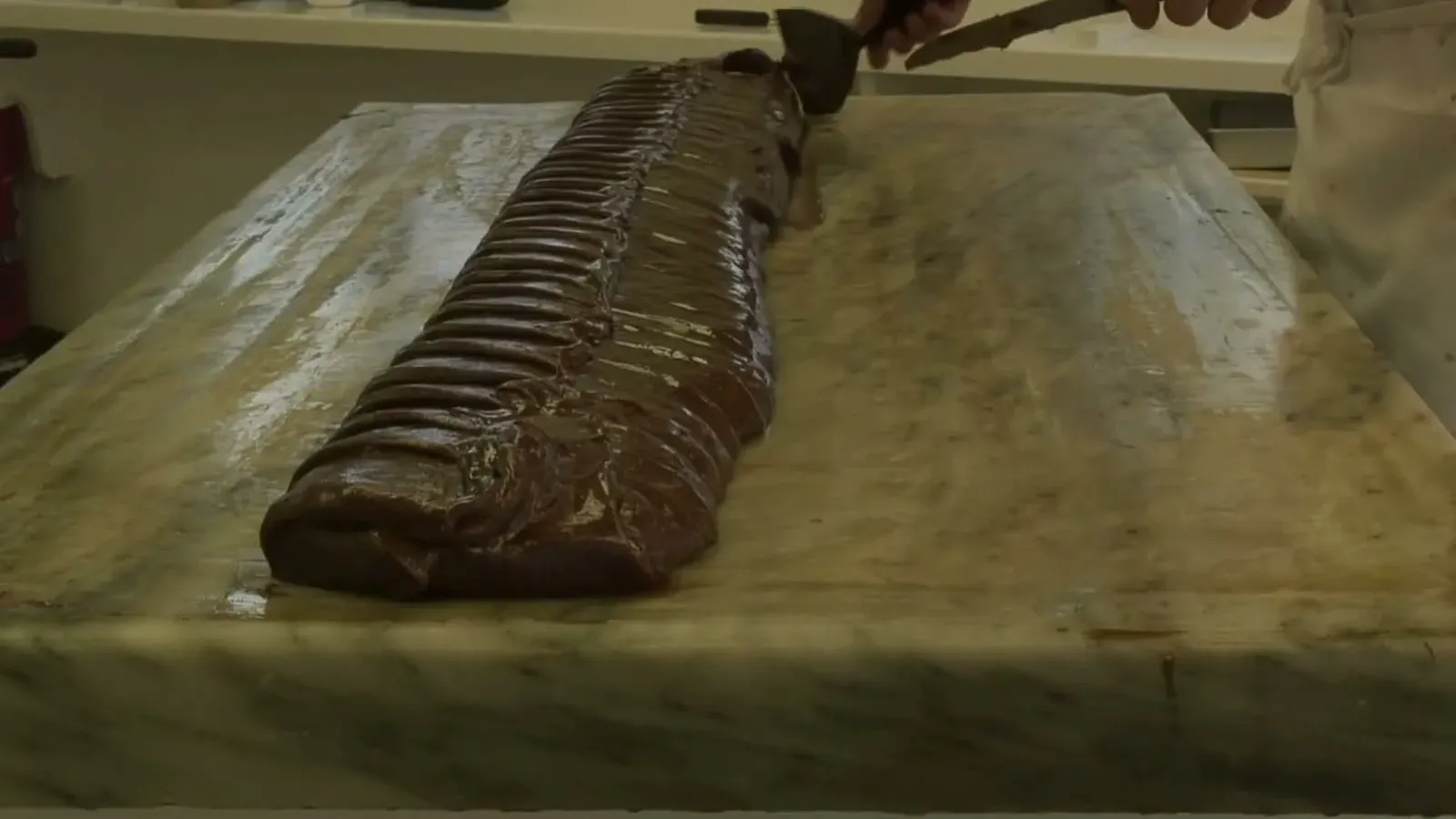 A fresh loaf of fudge being sliced on the marble slab in a Mackinac Island shop window.
