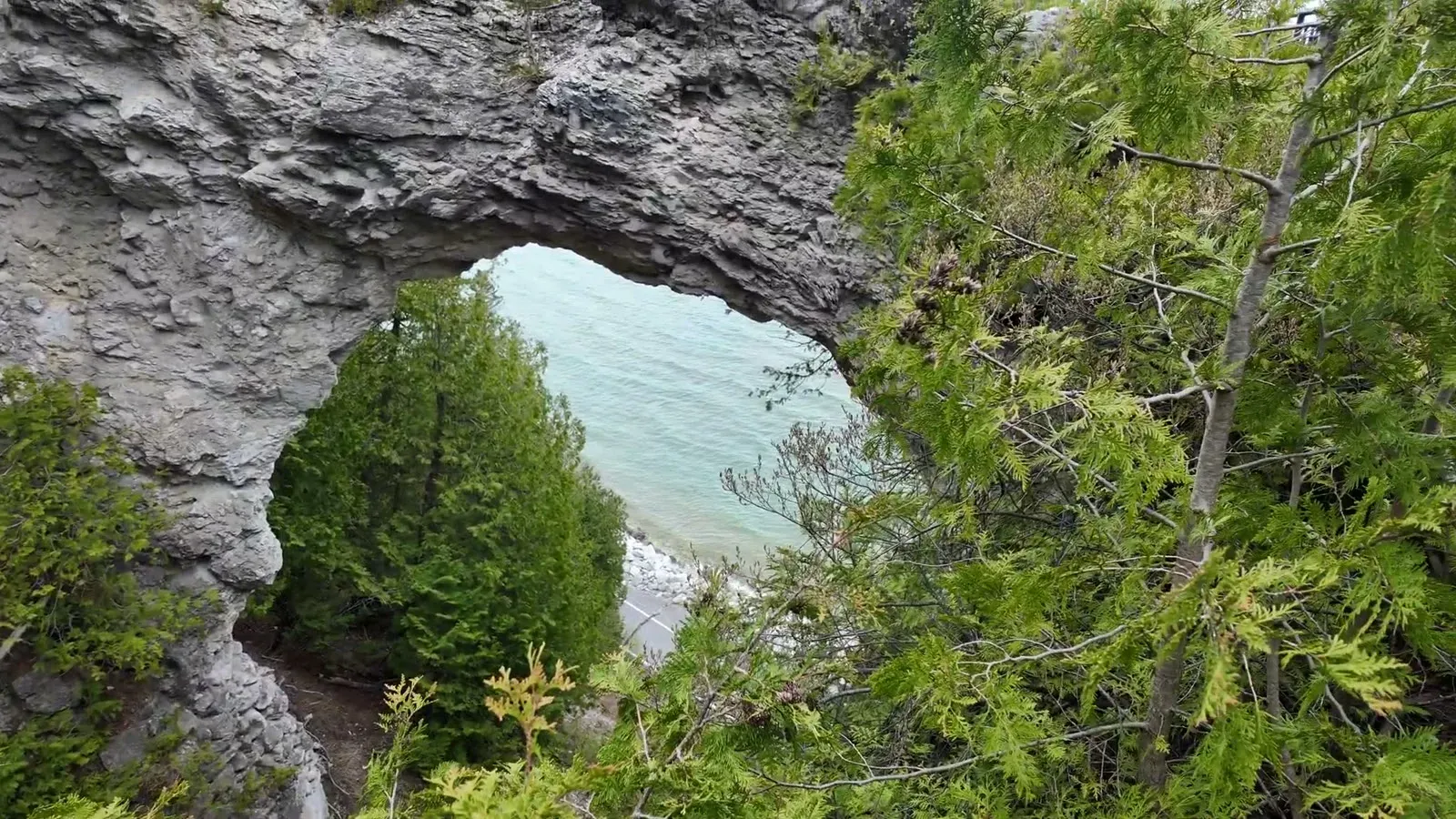 Arch Rock framing the turquoise water of Lake Huron far below, seen through the cedars at the top of the stairs.