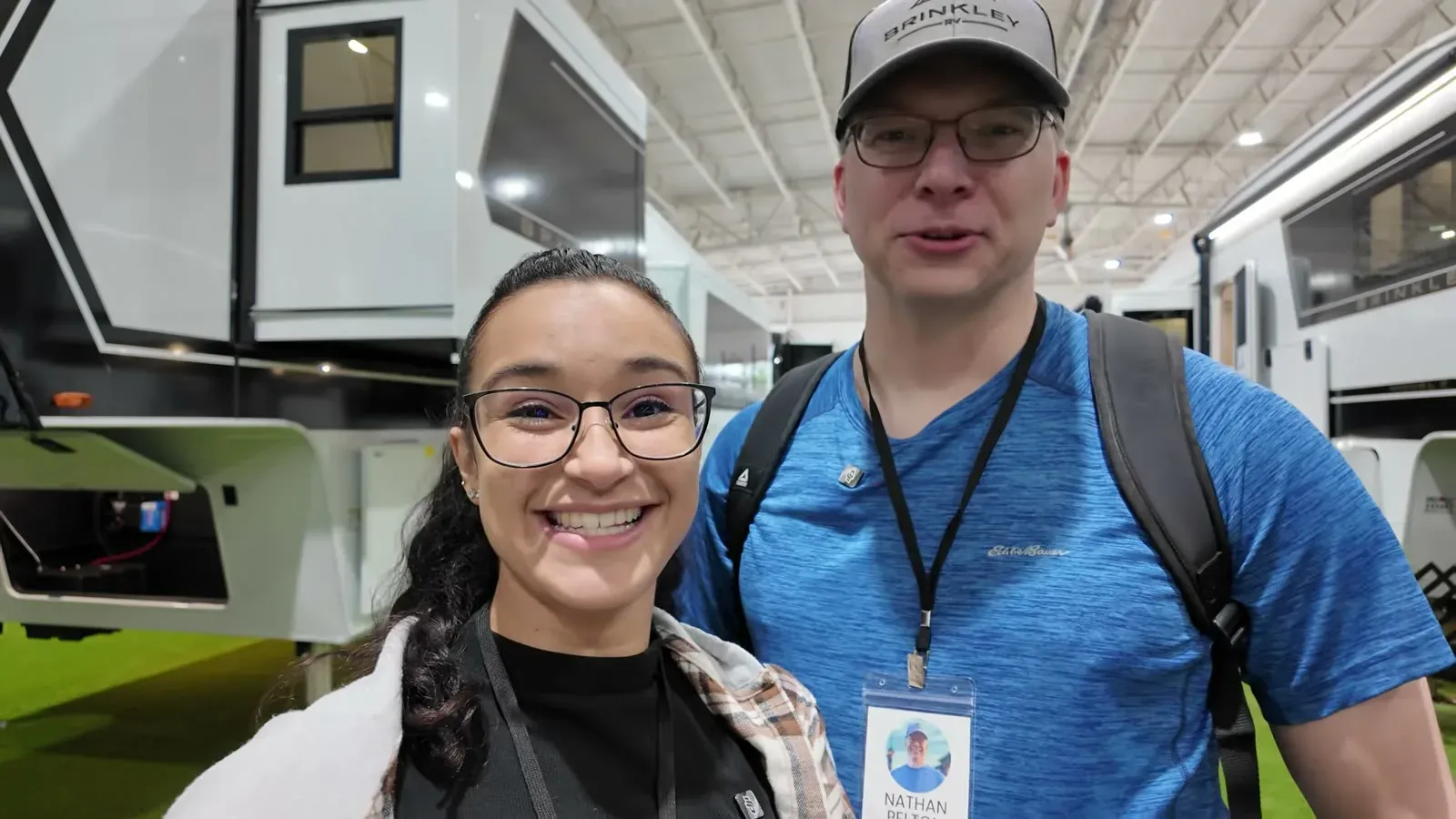 Nathan and Fabiola smiling in the Brinkley display hall at the Tampa RV Super Show, rigs lined up behind them.