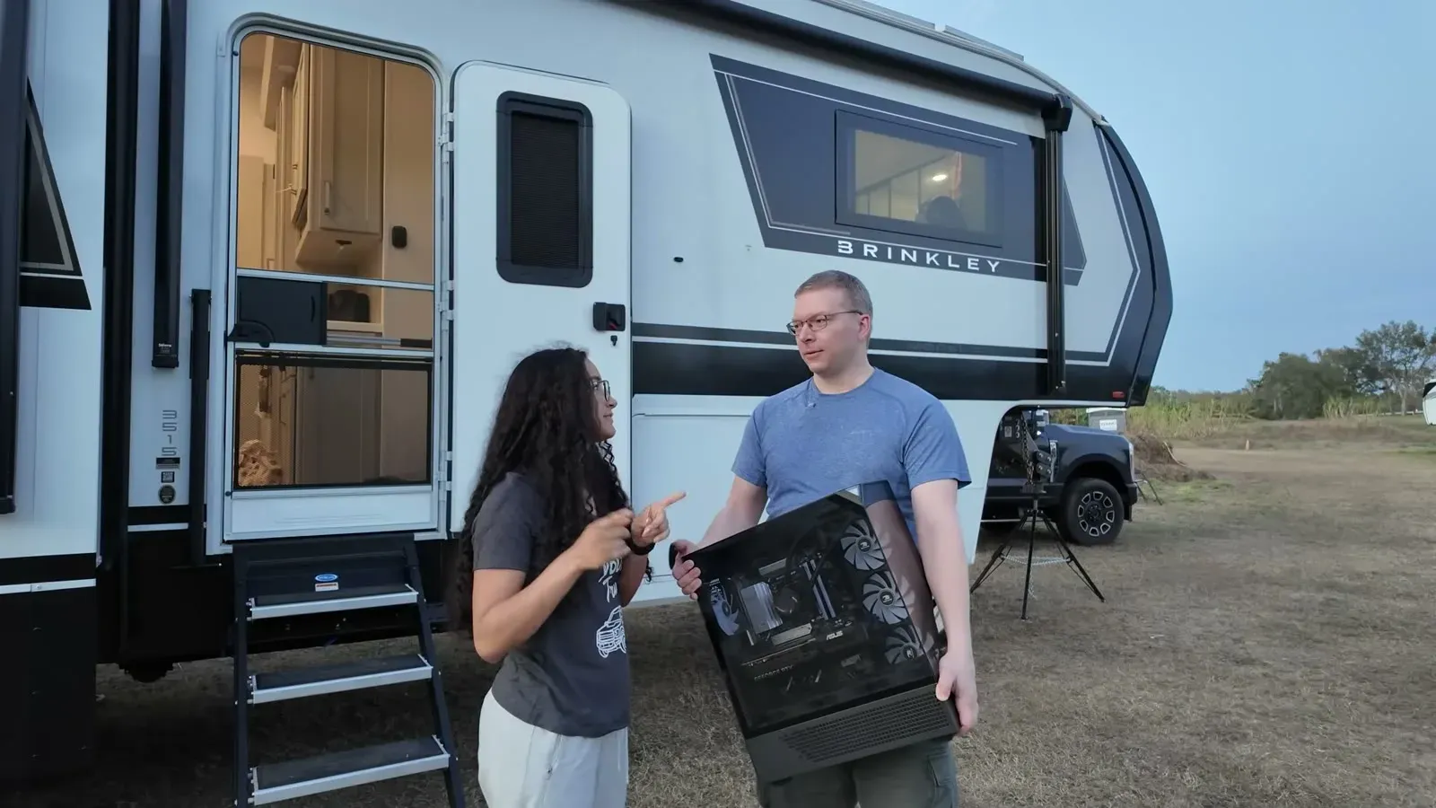 Nathan hauls the gaming PC out of the Brinkley under a gray Florida sky while Fabiola pleads the case for saving power.