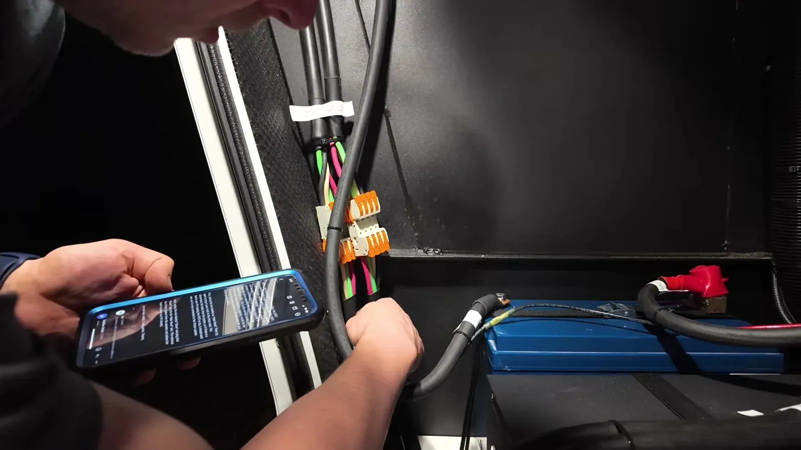 Following instructions on a phone while working through the wiring in the RV's battery compartment.