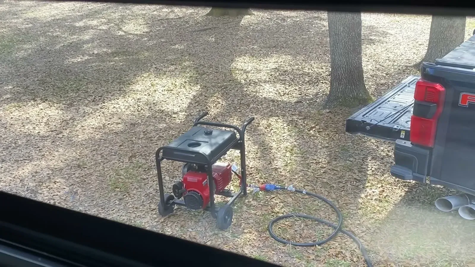 The neighbor's red generator running next to our F-350's tailgate with the cord run over to the RV.