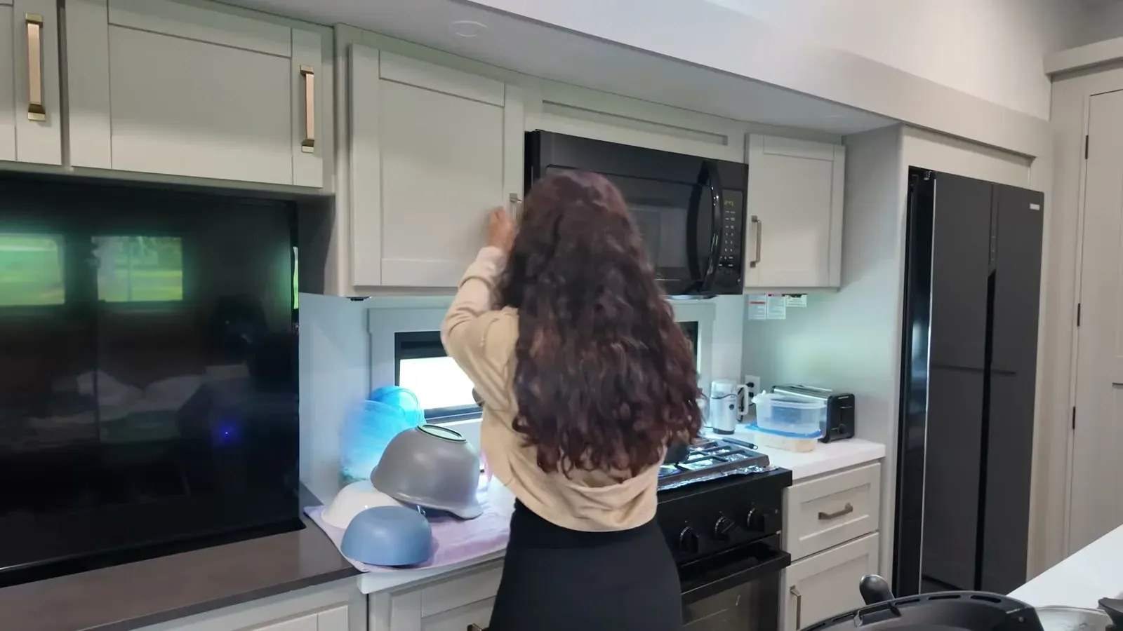 Fabiola putting clean dishes away in the camper kitchen, the unglamorous middle of a remote work week.